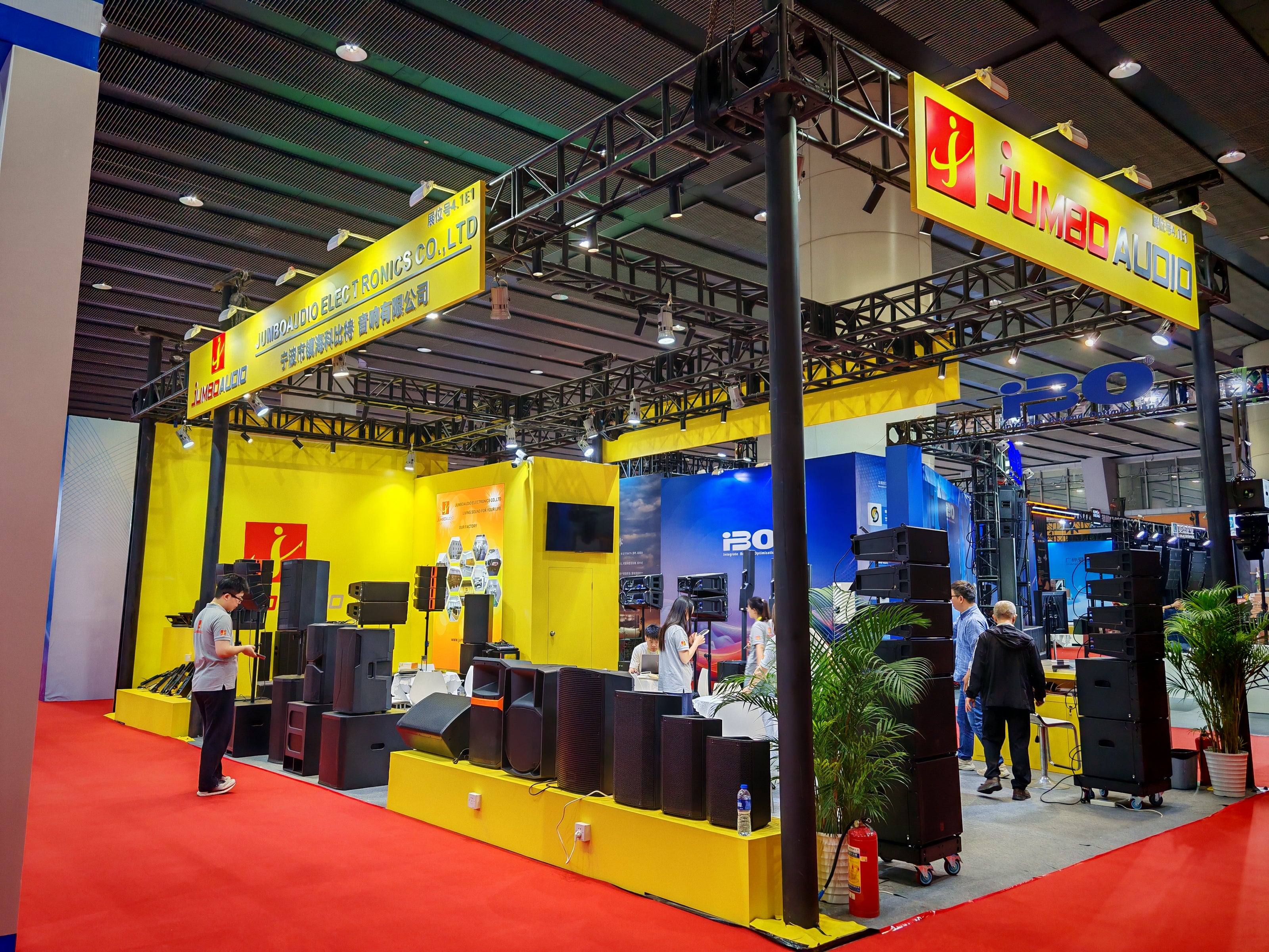 Large professional exhibition booth of Jumbo Audio at an international trade show, showcasing extensive lines of professional sound systems, line array speakers, and audio equipment