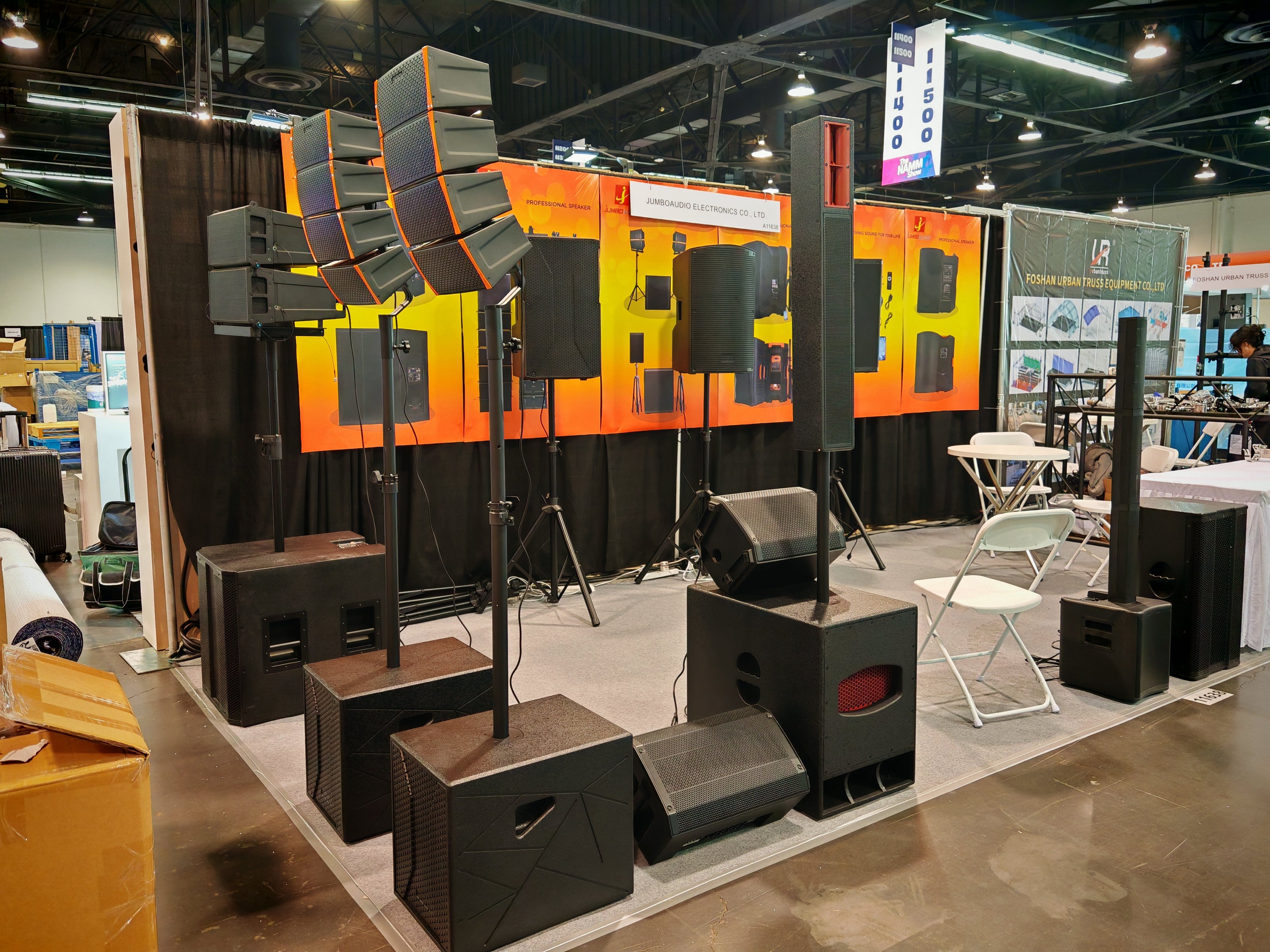 Trade show booth displaying large professional line array speakers, subwoofers, and high-power sound systems for live events and installations