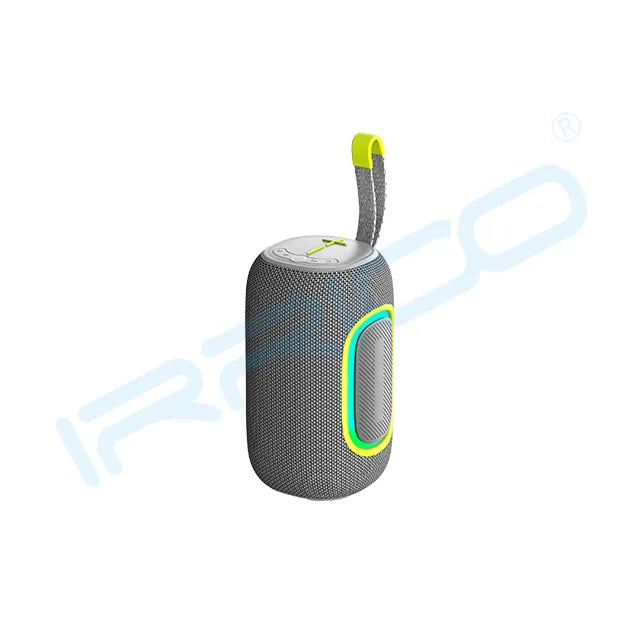 A grey cylindrical portable speaker with a textured fabric body, a glowing green and yellow oval light accent on the side, a top control panel, and a grey fabric carrying strap with a neon green accent