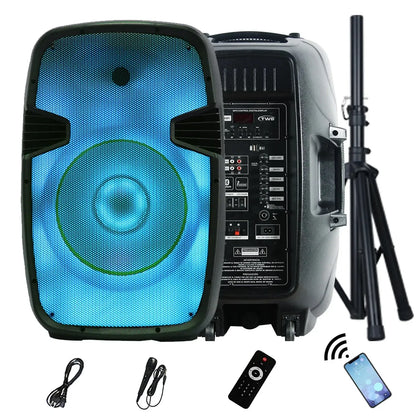 A portable PA speaker system with a large circular blue-lit driver on the front panel, showcasing a comprehensive control interface on the side with various input/output ports, knobs, and a digital display. The setup includes a remote control, a wired microphone, an audio cable, a smartphone indicating Bluetooth connectivity, and a telescopic tripod stand
