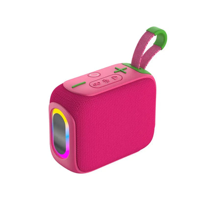 A hot pink rectangular portable speaker with a textured fabric body, a colorful glowing RGB light ring around the front speaker grill, control buttons on the top panel, and a pink fabric carrying strap with green accents.